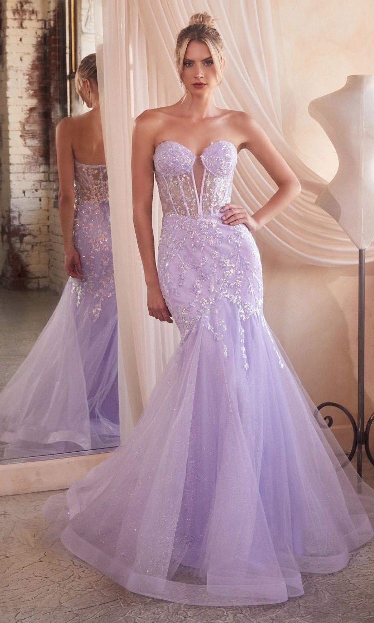 A woman in the Strapless Sweetheart Long Mermaid Prom Dress CB139, featuring a sheer bodice and floral embellishments, stands beside a mirror in a softly lit room.